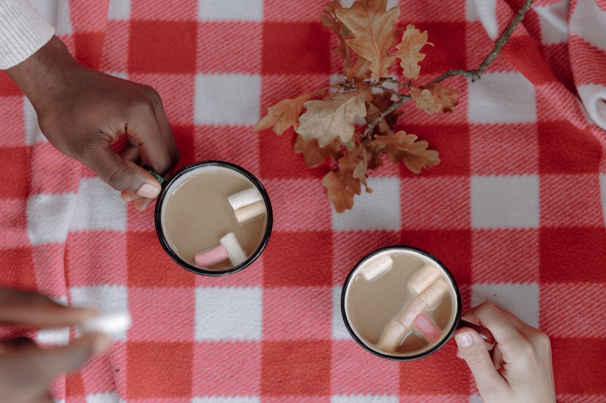 Two hands holding ceramic coffee mugs across a wooden table during a conversation.