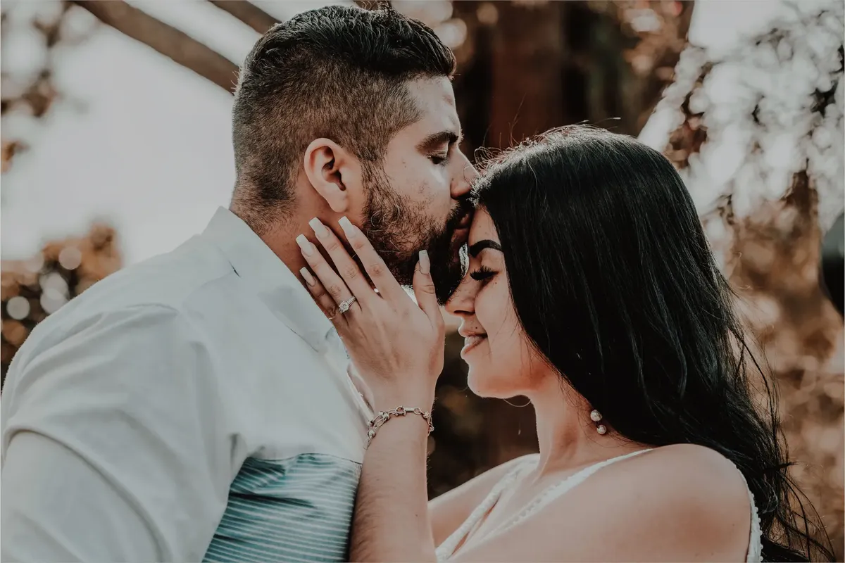 Tender moment of a couple sharing a forehead kiss outdoors, capturing love and serenity.