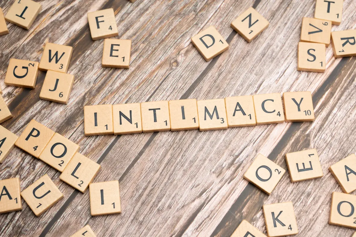 Scrabble tiles arranged to form the word 'intimacy' on a wooden background.