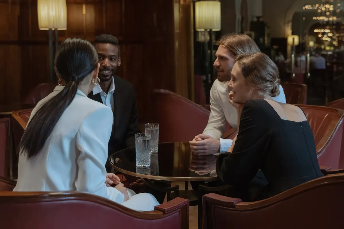A diverse group of adults sharing a friendly conversation in a warm, elegant lounge environment.