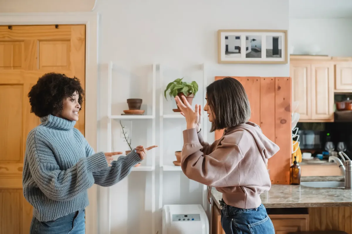 Side view of angry African American woman blaming and pointing at upset female while having dispute in modern light flat