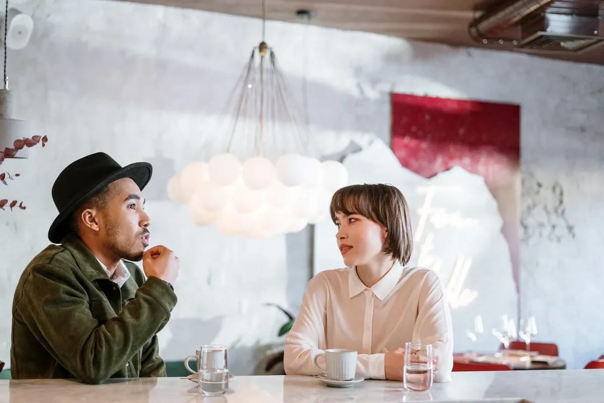 Two adults engage in a casual conversation in a stylish indoor café environment.