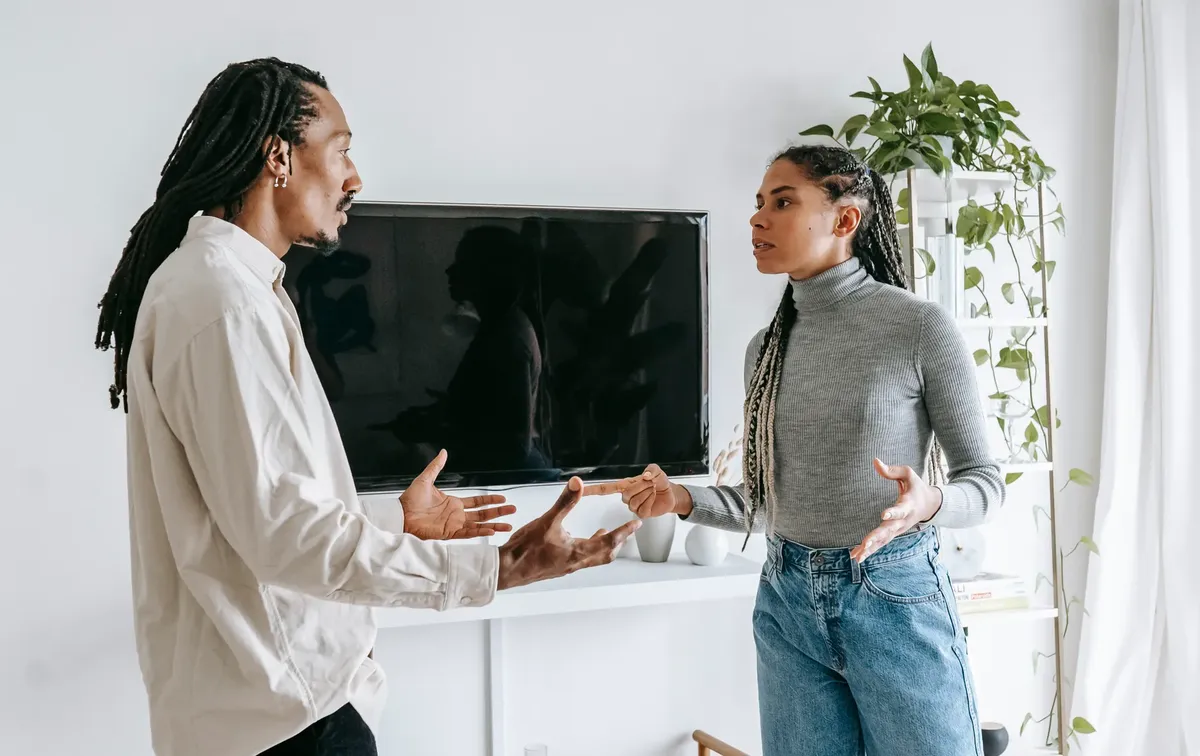 Side view of nervous young African American man and woman with dreadlocks in casual clothes quarreling together in light living room