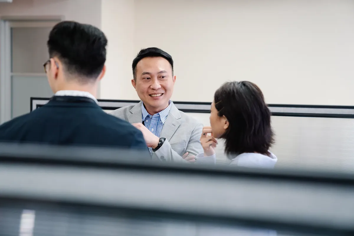 三名專業人士在辦公室環境中進行討論，分享想法與微笑。