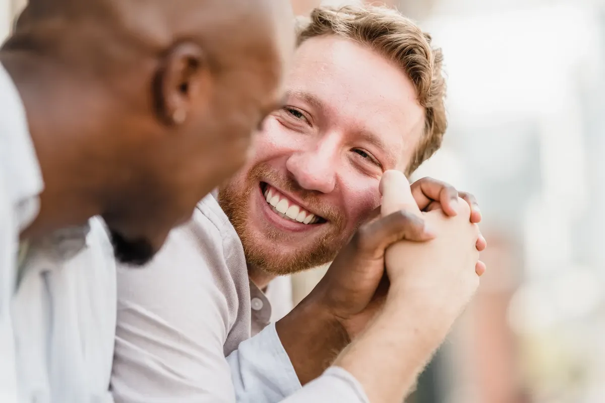 Two men sharing a joyful moment while holding hands and smiling warmly outdoors.
